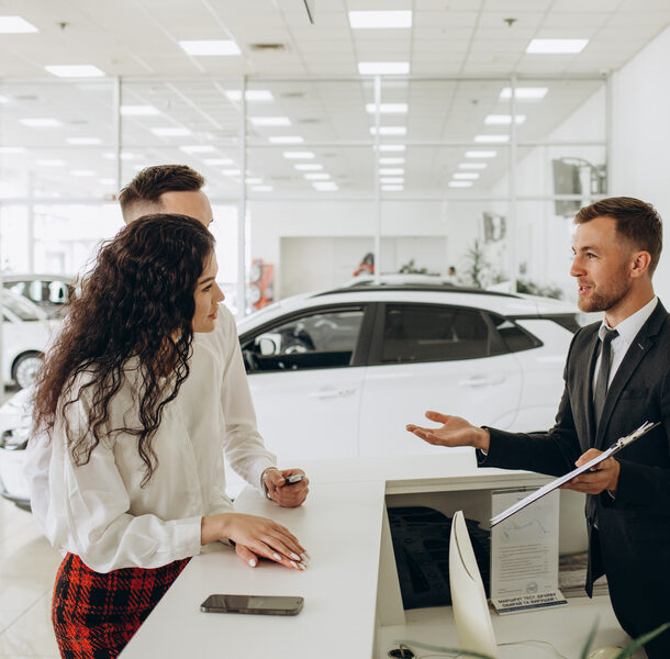 Sales manager showing car charging station to a young couple, selling electric cars in the showroom. Concept of buying eco-friendly car for family