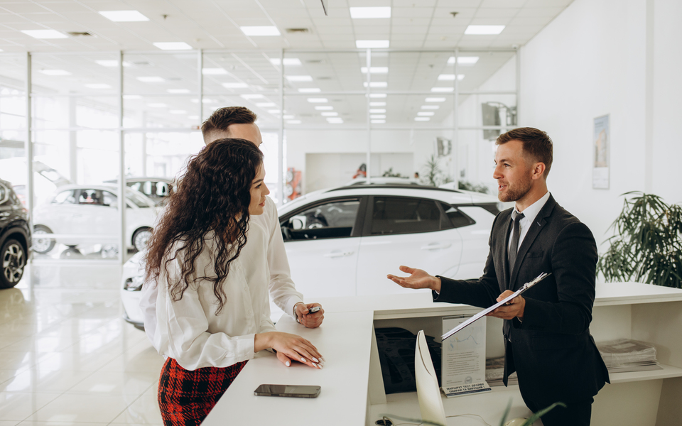 Sales manager showing car charging station to a young couple, selling electric cars in the showroom. Concept of buying eco-friendly car for family